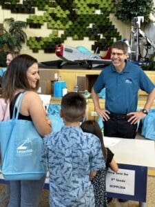 Student stands with school supplies and bag facing a teacher smiling.