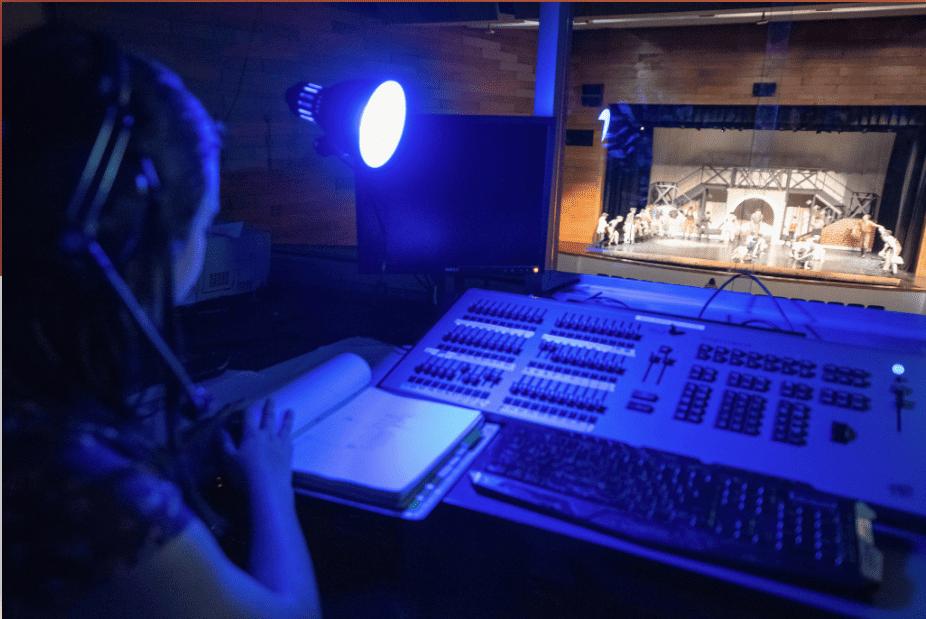 age of student sitting in a sound booth looking out on a stage