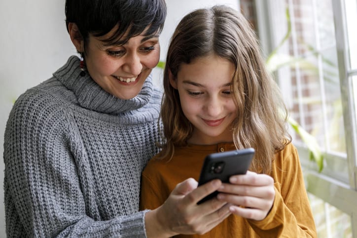 mother and teenager daughter at home using mobile phone. Lifestyle and technology indoors