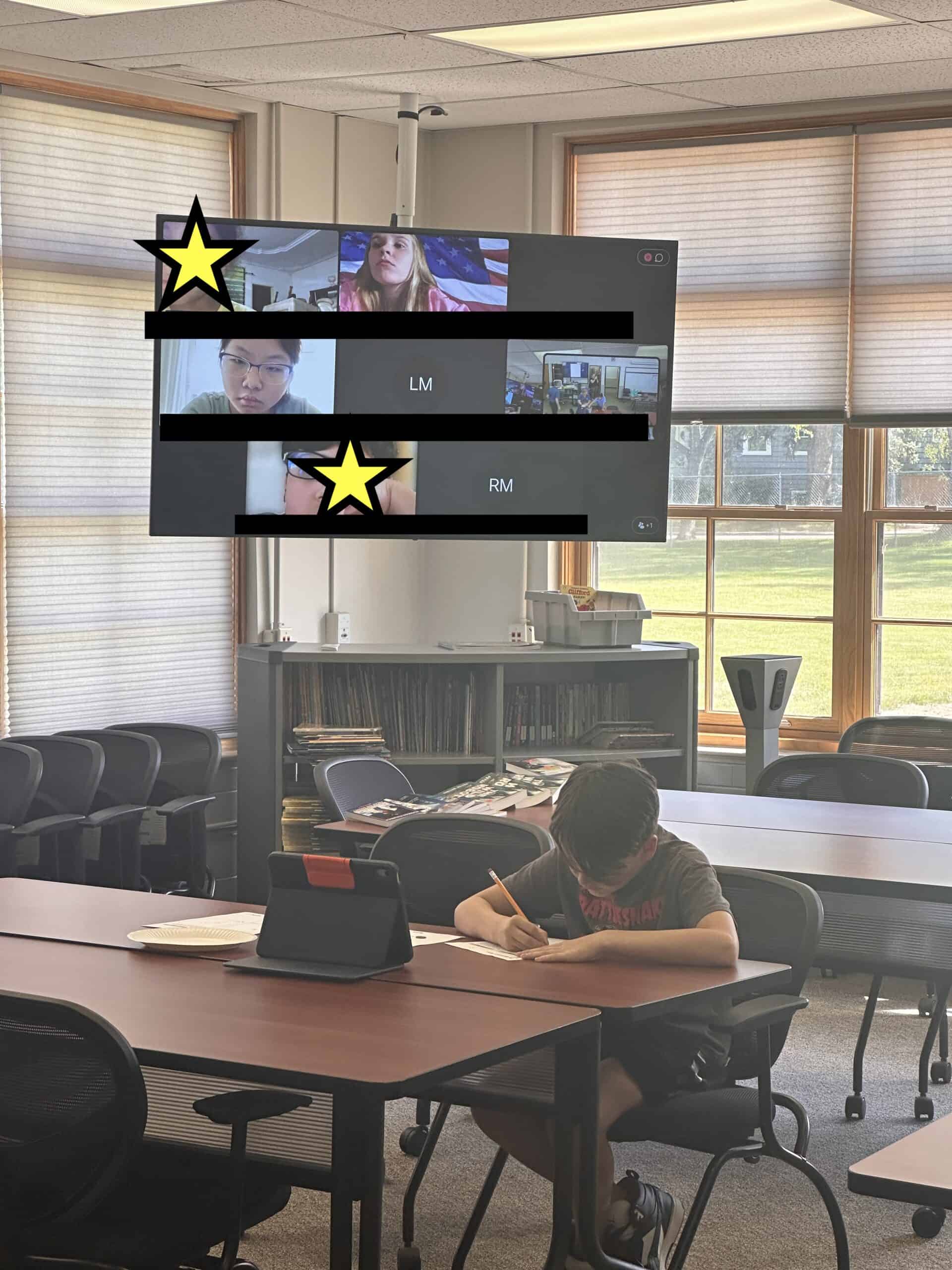 Student sits at iPad while other students look on in the background from a virtual meeting screen