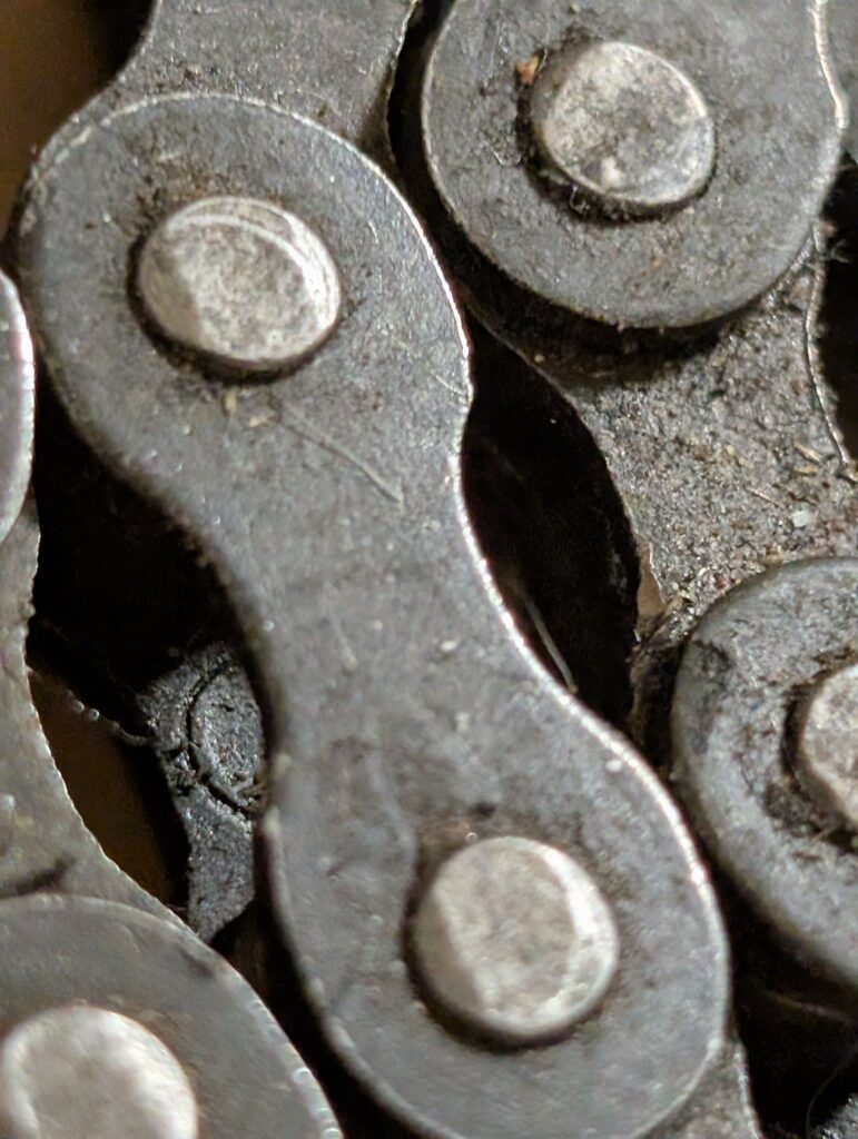 Close-up of a bicycle chain, showing metal links and connecting pins with a slightly worn texture.